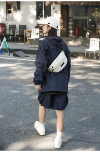 Outdoor street style view of a white lightweight chest bag with adjustable black strap