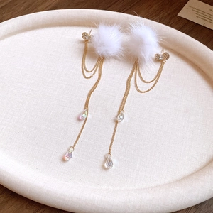 Detail of plush ball earrings with gold chain and clear teardrop pendant on a tray