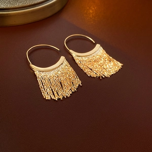 Detail of elegant gold C-shaped fringe tassel earrings on premium leather texture