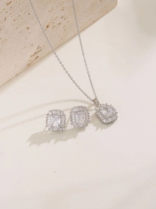 Elegant jewelry set with silver necklace and square zircon earrings on stone surface