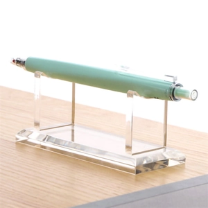 Macro side view of clear acrylic pen display stand on a light wood desk background