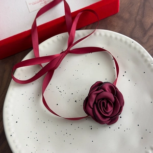 Detail of burgundy satin rose choker necklace with elegant long ribbon on a ceramic plate
