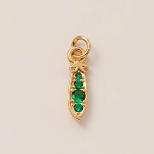 Close-up of golden pea pod pendant with four green round gemstones on beige background