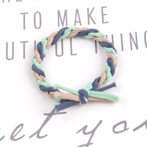 Detail of hand-woven green blue and beige braided hair tie on a white display card