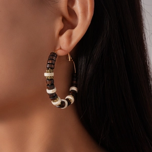 Macro detail of large hoop earring featuring dark wood and gold metallic beads