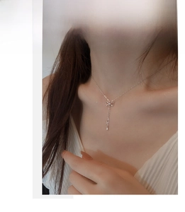 Detail of silver bow tassel necklace on model showing delicate fringe and dainty charms