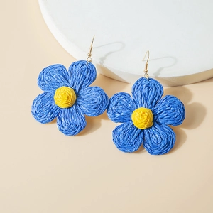 Detail of handmade raffia flower earrings with blue petals and yellow center on gold hooks