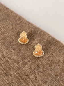 Detailed close-up of gold-plated gourd stud earrings with orange gems and white zircon inlay