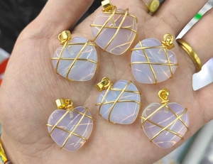 Detailed macro of six handmade opal heart pendants with gold wire wrapping on palm