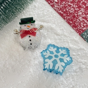 Close-up of glittery acrylic snowman and snowflake hair claw clips on snowy background