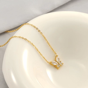 Macro shot of a 18k gold butterfly necklace with marquise-cut zircons in a ceramic bowl