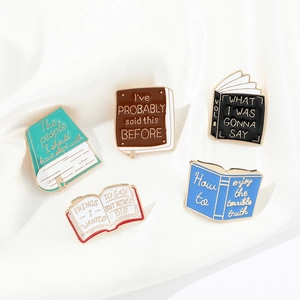 Detailed close-up of 5 enamel book pins with creative quotes on soft white fabric