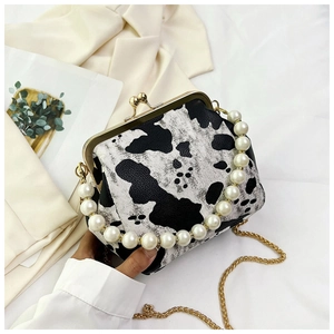 Detail of cow print handbag featuring pearl handle and gold chain shoulder strap