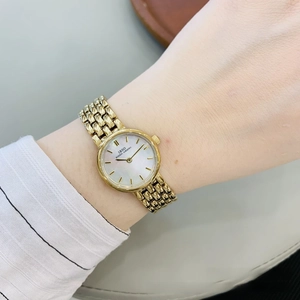 Detailed close-up of a women's gold metal watch with a white mother of pearl dial face