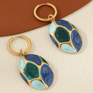 Macro shot of oval gold-plated earrings with multicolored blue and green enamel inlay