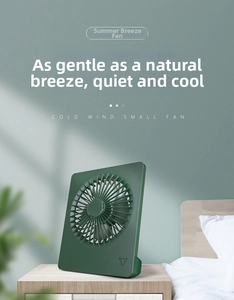 Close-up of a dark green desktop fan with square frame on a wooden nightstand