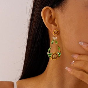 Close-up of golden sunflower earrings with bee accents and green beads on model