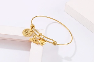 Detail of adjustable gold bracelet with heart and MOM pendants on white display