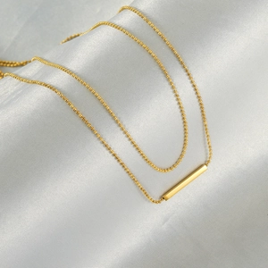 Double-layered golden bead chain necklace featuring a minimalist vertical bar pendant