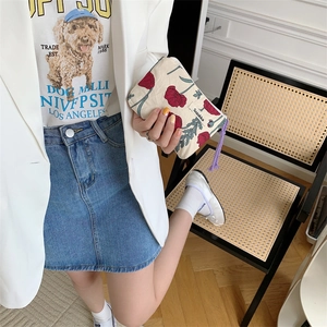 Beige canvas makeup bag with red poppy print and purple zipper held by a model