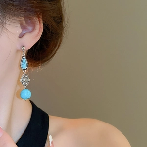 Detail of vintage turquoise drop earrings featuring embossed silver flowers on a model