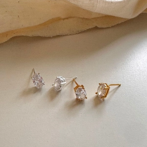 Detail of oval-cut gold and silver stud earrings with four-prong settings on fabric
