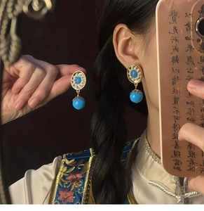 Detailed close-up of retro gold-framed oval earrings with blue beads and small pearls