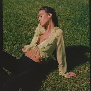 Detail of light green sheer long sleeve top with ruffles and front tie design in sunlight