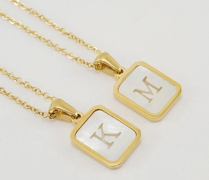 Detailed macro view of 18K gold-plated square pendants with shell inlay and letters M and K