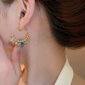 Close-up of bohemian gold hoop earrings with multi-colored stones on a female model