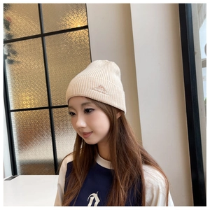 Close-up of a stylish cream knitted beanie worn by a model in a modern indoor setting