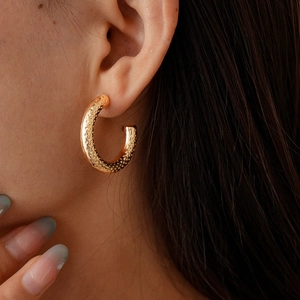 Macro shot of gold C-shaped earrings featuring hammered texture and vintage metallic finish