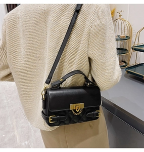 Detail of black quilted crossbody bag featuring a golden metal lock and chain strap accents