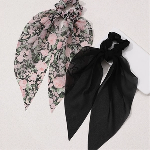 Detail showing two chiffon ribbon scrunchies in solid black and floral pattern on light surface