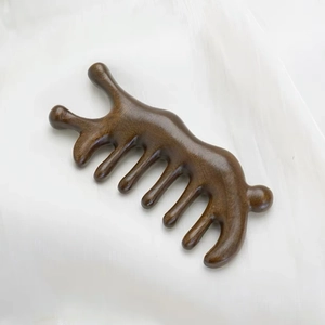 Macro shot of polished sandalwood meridian massage comb with five smooth teeth on white silk