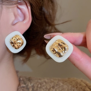 Close-up of square hammered gold stud earrings with white acetate frame on ear