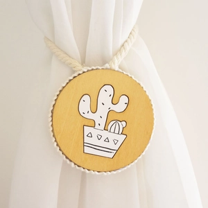 Detail of wooden curtain tieback featuring a hand-painted cactus motif and cotton rope