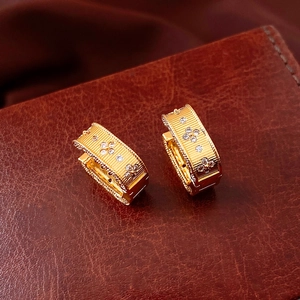 Detail of vintage gold textured earrings with zircon floral patterns on leather