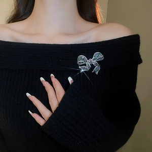 Close-up of a bow brooch with purple and green zircons on a black sweater fabric