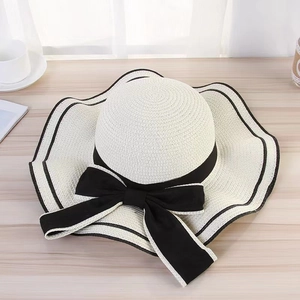 Top view of a cream straw sun hat featuring a wide black bow and elegant wavy brim