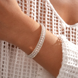Detailed view of layered faux pearl and rhinestone bracelets on a model wrist
