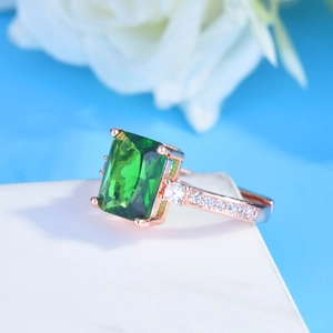 Close-up of rectangle green emerald ring with rose gold band and pavé diamonds