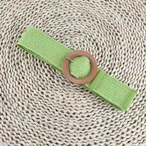 Detail of light green woven belt featuring a round wooden buckle and fine texture