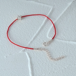 Macro shot of minimalist red rope bracelet with silver clover charm and sparkling zircon
