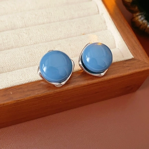Dettaglio ravvicinato di orecchini tondi blu con base argento su vassoio in legno