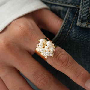 Macro detail of a wide gold ring with vintage pearl clusters on a hand model