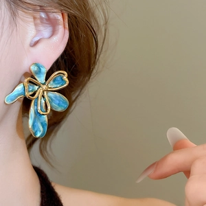 Dettaglio dell'orecchino vintage a fiore blu con bordo dorato indossato su modella