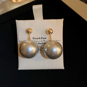 Detailed shot of large grey pearl drop earrings with gold ball studs on a French display card