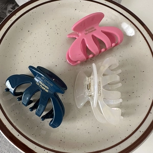 Close-up of pastel pink, navy, and clear oval hair claws on a ceramic plate