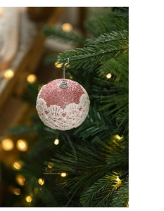 Close-up of pink glitter Christmas ball with white lace hanging on a green tree branch
